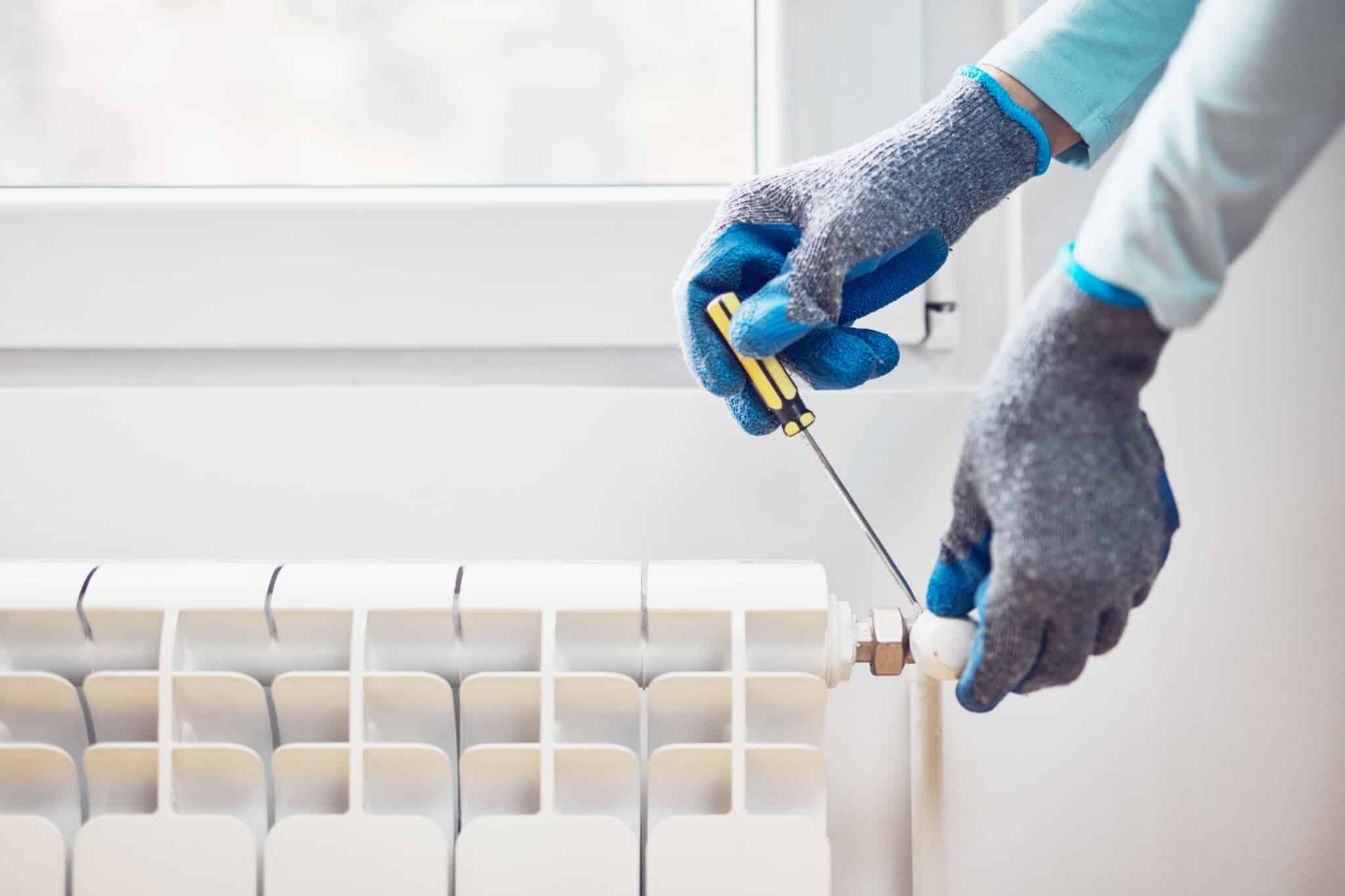 Handyman with gloves fixing and bleeding air from central heating gas radiator system at home, Radiator Bleeding.