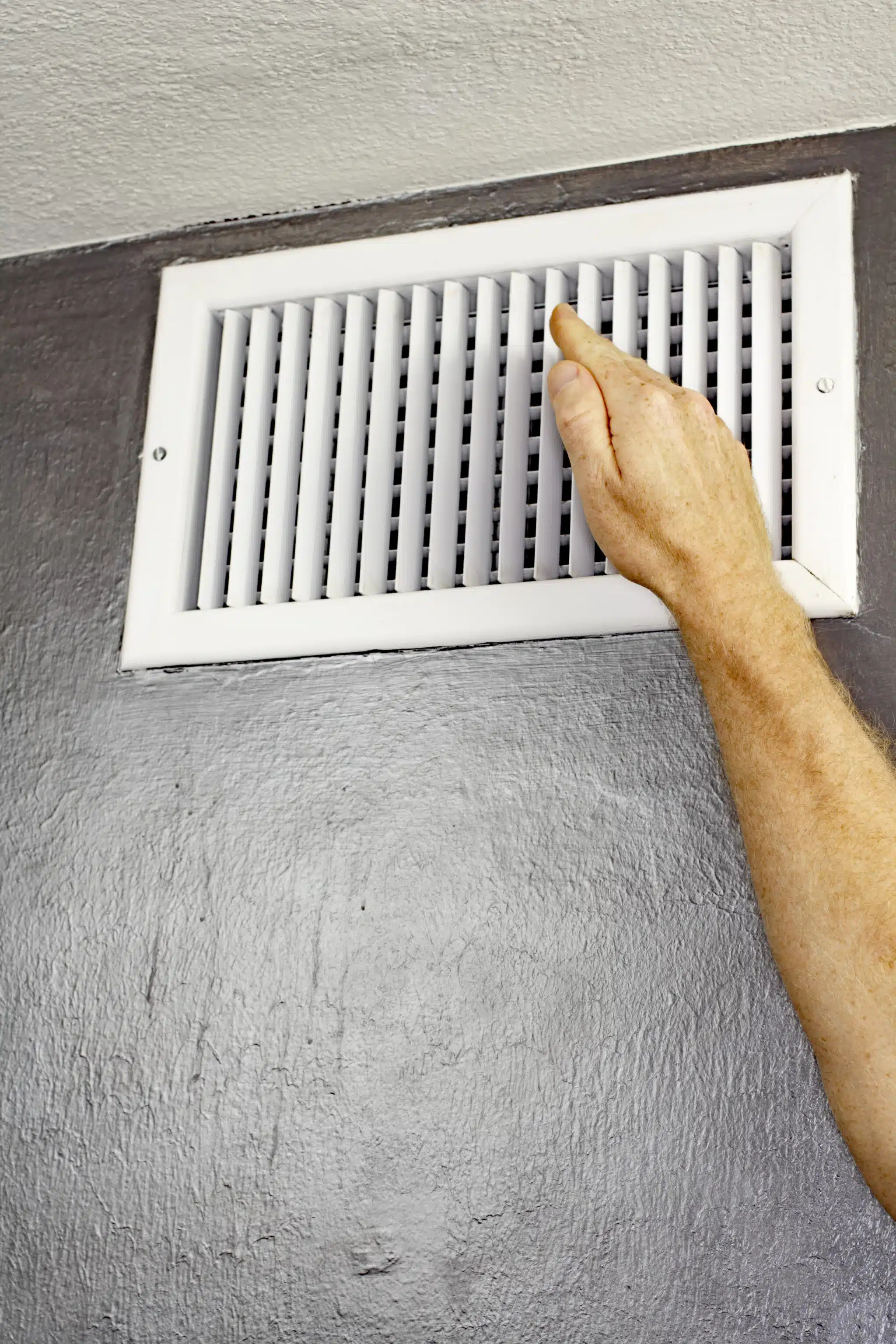 A man holding a hand up in front of an air vent checking the air temperature, Emergency Heat Mode.