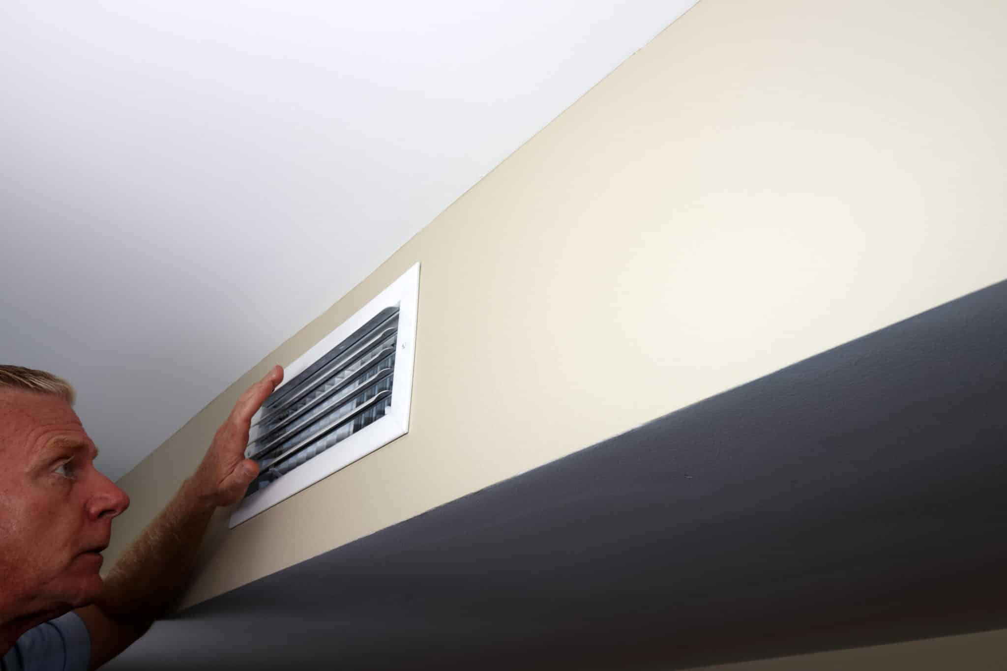 Man looking into a wall home air vent, Prevent Heat Loss.