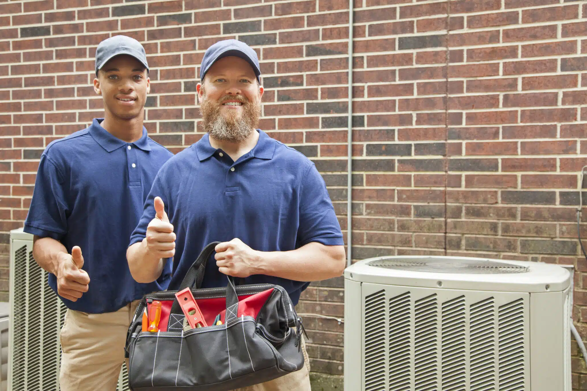 Air conditioner repairmen work on home unit. Tool bag, HVAC Contractor.